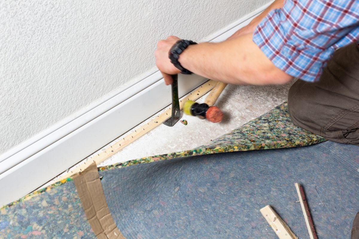 A man uses a hammer to secure a carpet, demonstrating a step in carpet installation and maintenance.