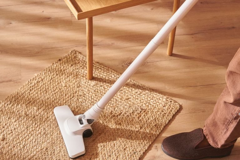 A person vacuuming a rug, demonstrating effective carpet cleaning techniques in a well-lit room.